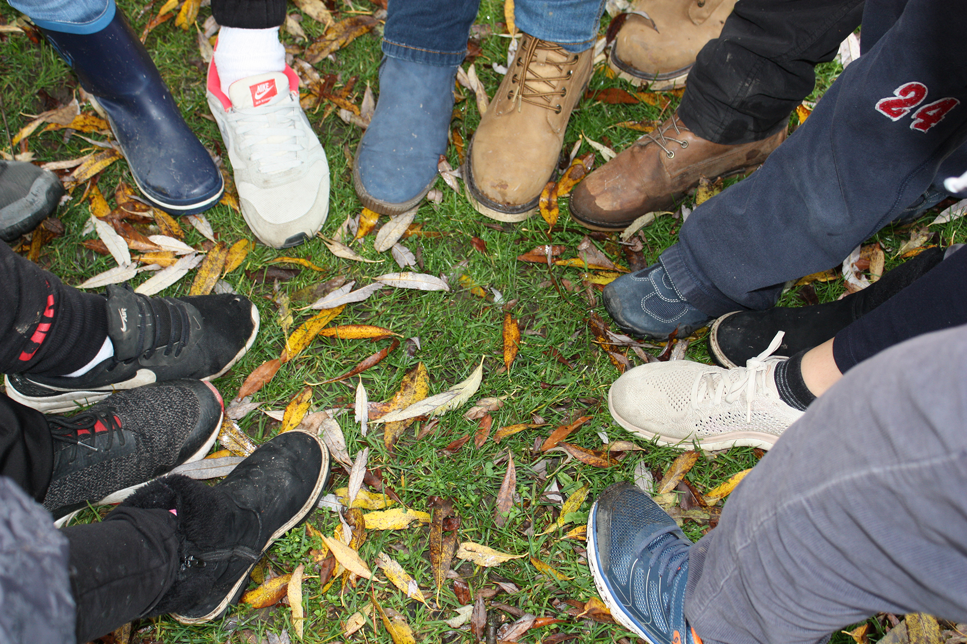 Im Bild: mehr als zehn Personen bilden mit ihren Schuhen einen Kreis auf einer herbstlichen Wiese.