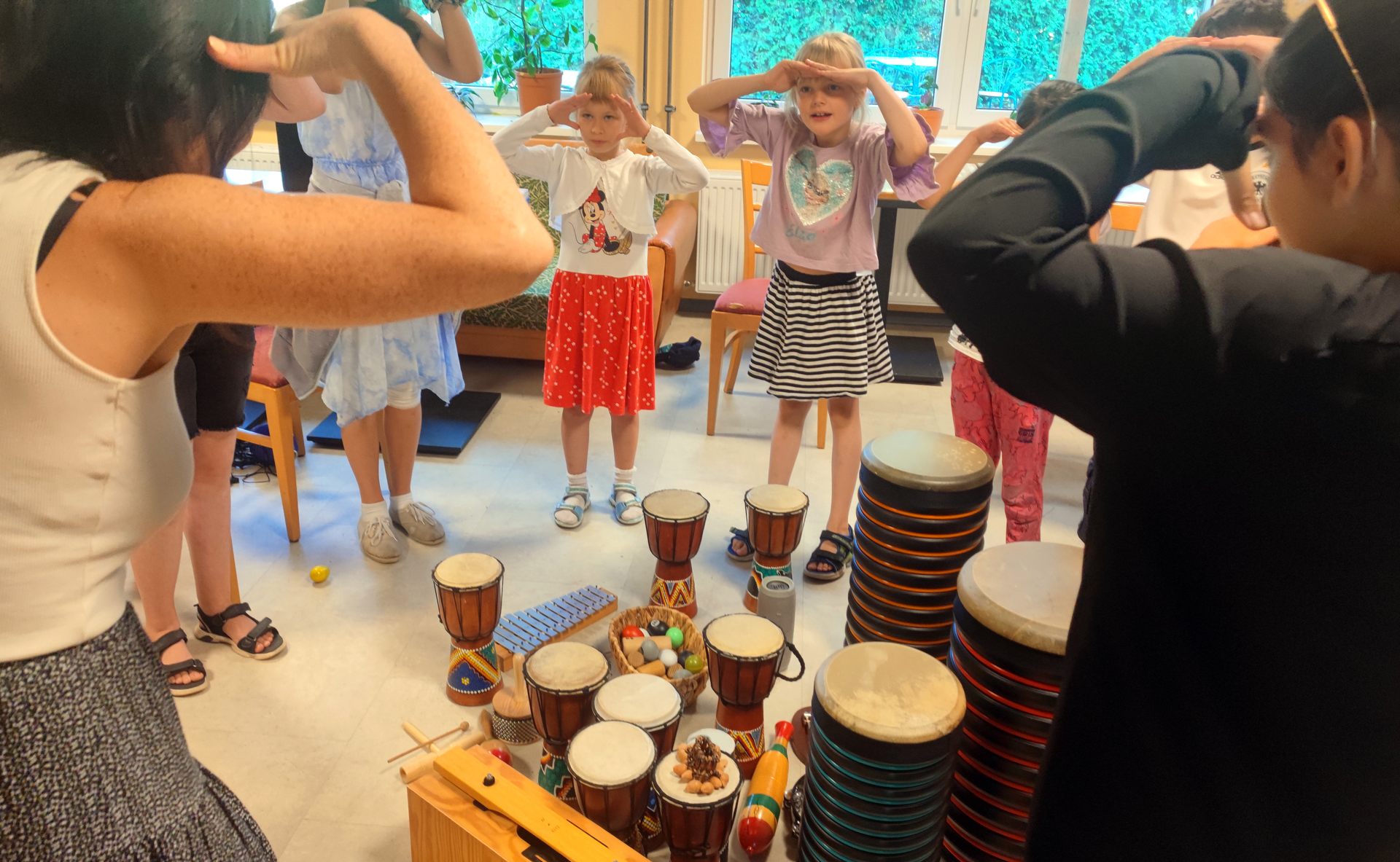 Eine Gruppe von Kindern steht im Kreis um Musikinstrumente herum. Alle halten die Hände wie einen Sonnenschirm über den Augen und gucken konzentriert.