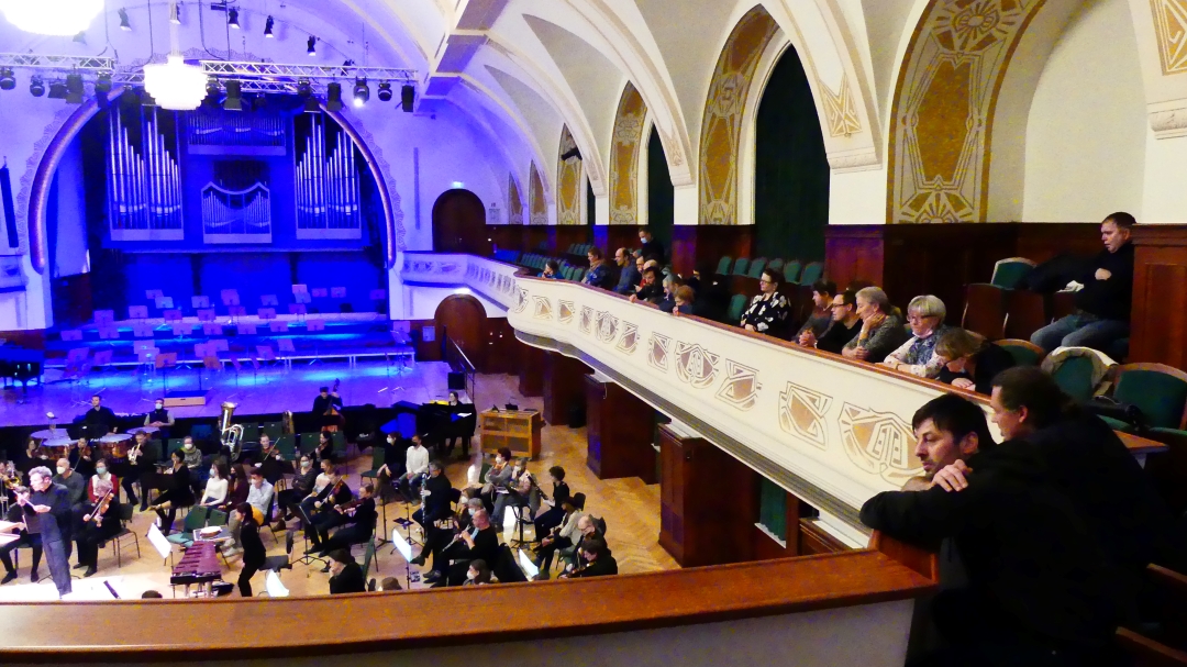 Blick auf auf ein Orchester in einer großen historischen Konzerthalle. Die Beleuchtung ist blau.