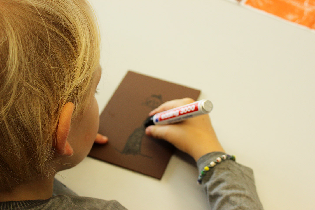 Im Bild zu sehen ist: ein kleines Kind malt mit einem Stift auf einen Karton.
