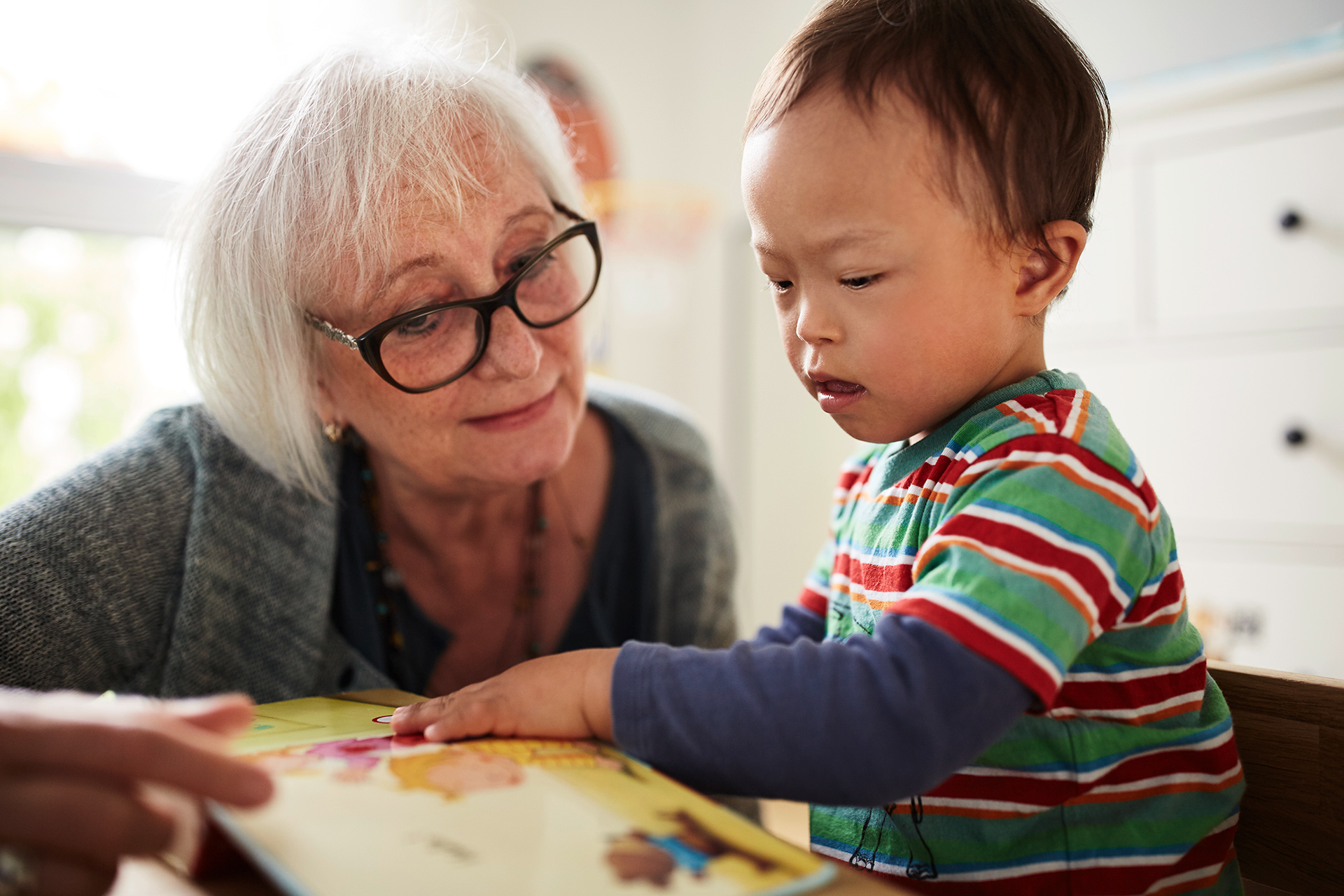 Im Bild ist eine ältere Betreuerin, die gemeinsam mit einem Kleinkind ein Buch anschaut.