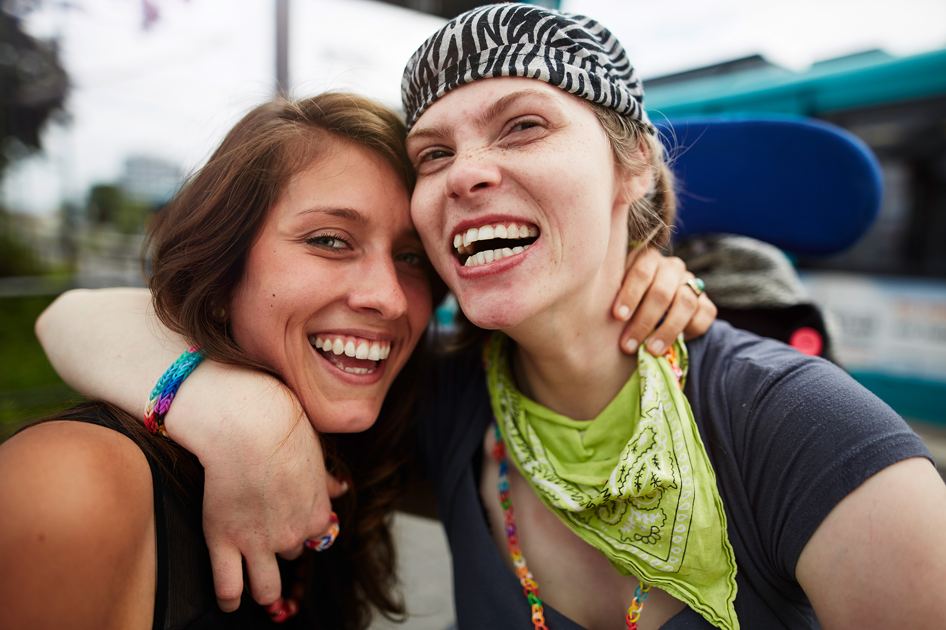 Im Bild: eine junge lächelnde Frau Arm in Arm mit junger Frau mit Handicap