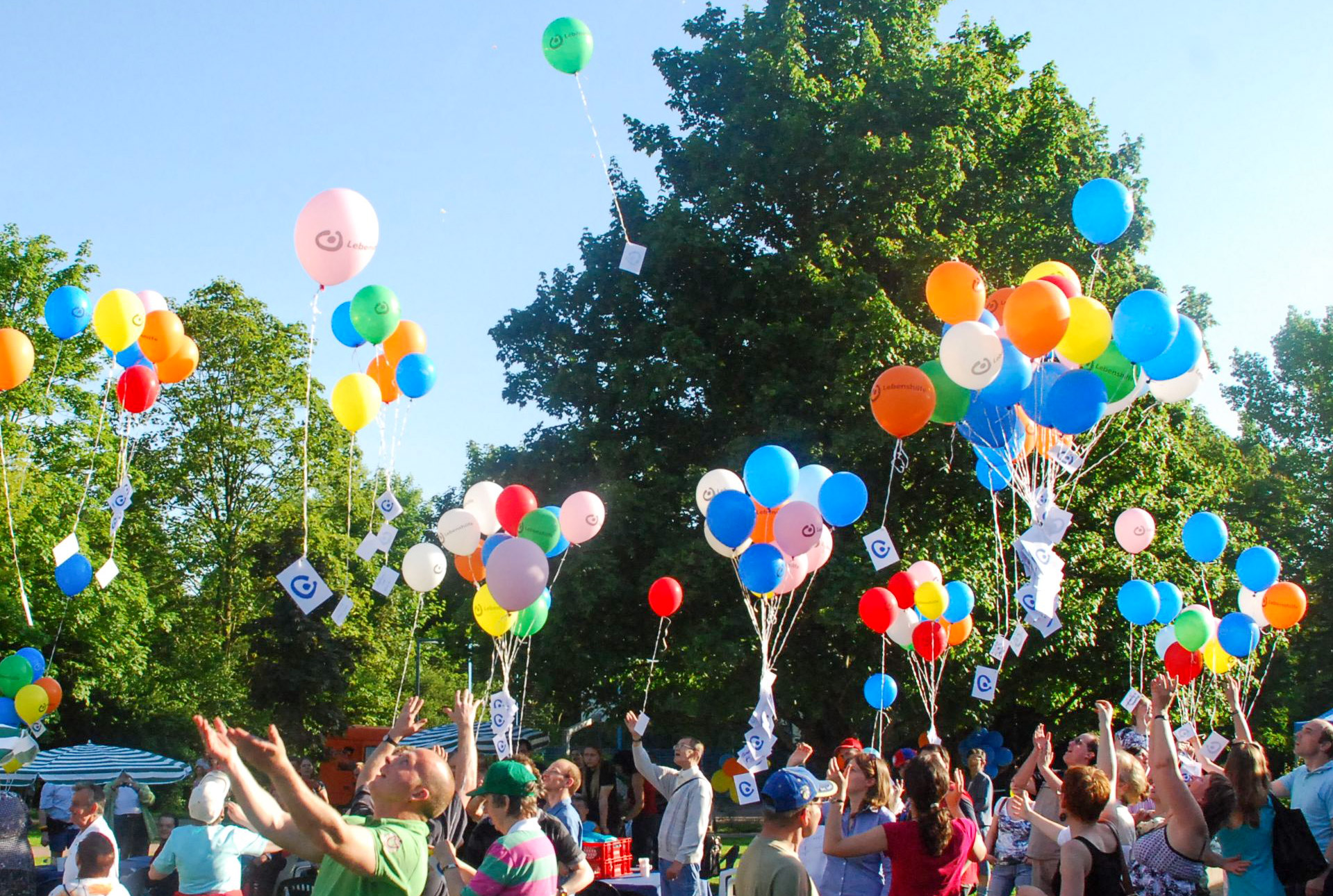 Ein Symbolfoto: viele Menschen lassen bunte Luftballons in den Himmel steigen.